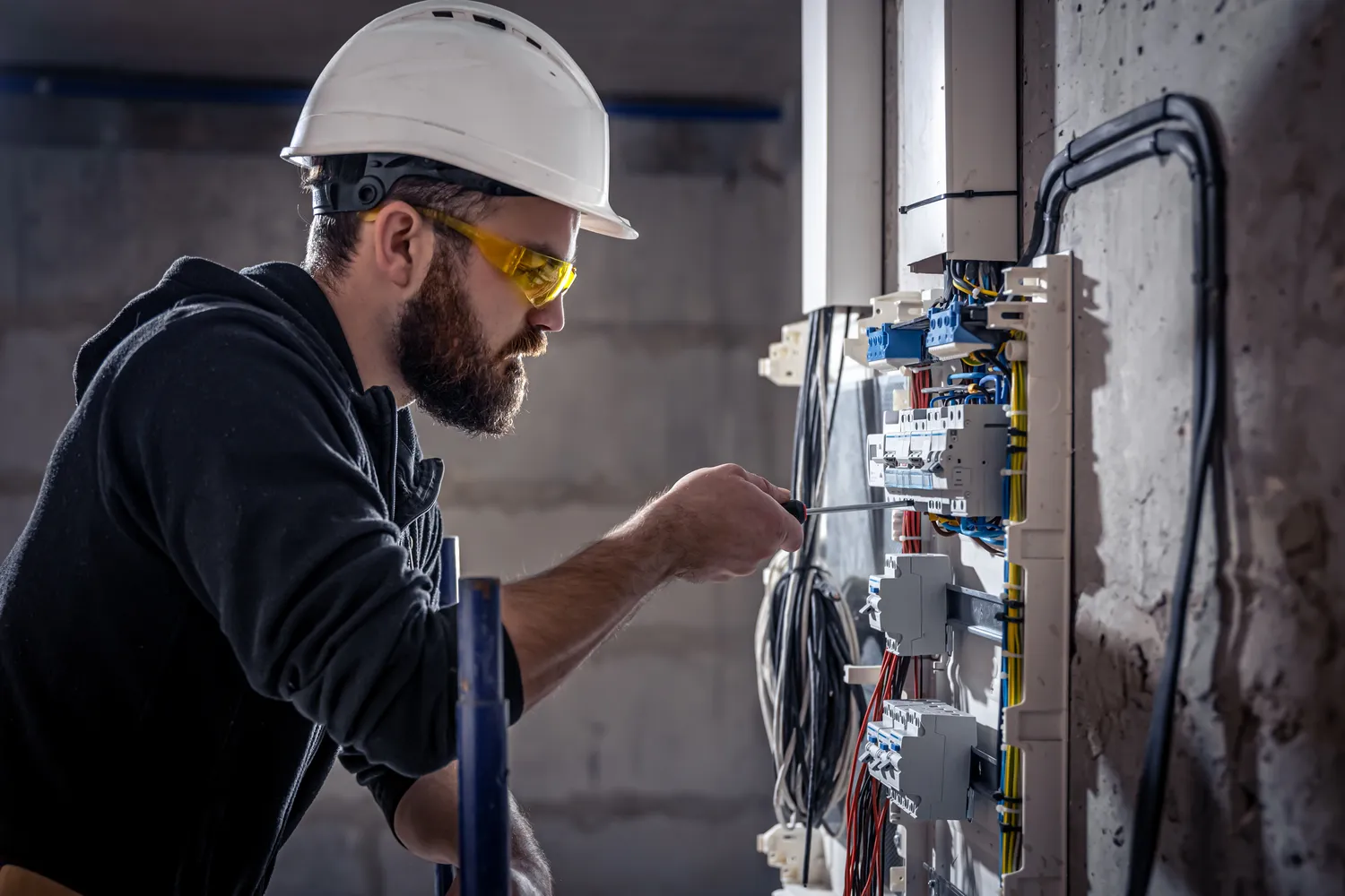 Pötschke Elektro - Elektrofachunternehmen - Ein männlicher Elektriker arbeitet an einem Verteilerkasten mit einem elektrischen Verbindungskabel.