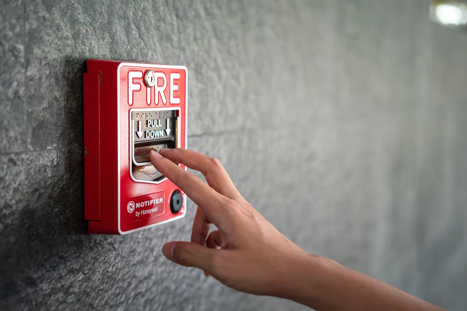 Pötschke Elektro - Elektrofachunternehmen - Aktivierung der an der Granitwand des Gebäudes installierten Feuermeldeanlage. Foto einer Szene mit Personenkontakt, selektiver Fokus.